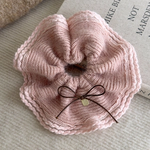 Close-up of pink knitted scrunchie featuring a brown bow and small metallic pendant detail