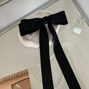 Oversized black satin bow hair clip with long ribbons on a white ceramic plate