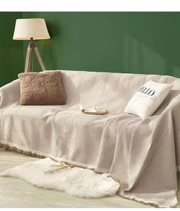Detail of beige waffle weave sofa throw blanket with decorative fringe on a couch