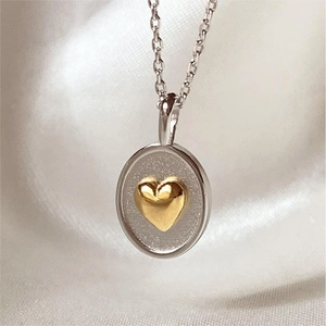 Two-tone heart oval pendant necklace in 18k gold plating on white silk backdrop