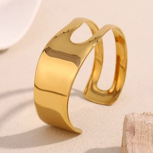 Detailed view of wide gold open cuff bracelet with geometric cutout on sand texture