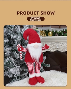 Detail of knitted Christmas gnome figure with candy cane standing by festive fireplace