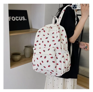 Detail of white corduroy backpack with strawberry print worn by a model in a cozy setting