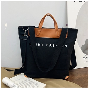 Detail of black canvas tote bag with brown leather handles and adjustable shoulder strap