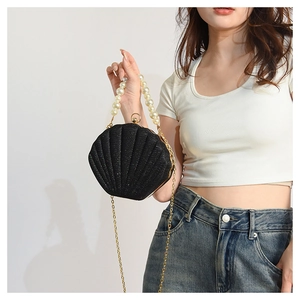 Detail of black shell bag featuring sparkling texture, pearl handle, and metal chain strap
