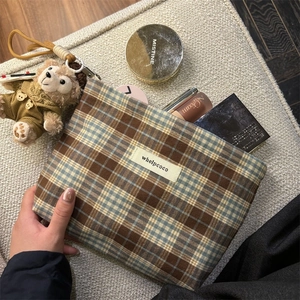 Detail of checkered fabric pouch in brown and blue with zip closure and brand label