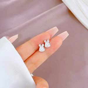 Close-up of minimalist silver rabbit stud earrings on finger showing small scale size