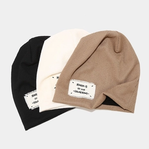 Three knitted slouchy beanies in black, cream, and khaki with stylish logo patch detail