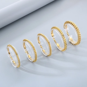 Detail of five woven wheat chain bracelets in gold finish on acrylic stands