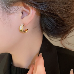 Close-up of C-shaped gold earrings with green gemstones and pearls on model
