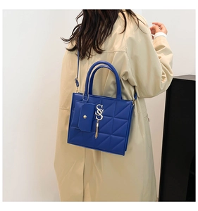 Dettaglio borsa blu trapuntata con logo S e nappa indossata su un trench beige