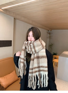 Detail of warm mohair plaid scarf with tassels worn by a model in a cozy cafe setting