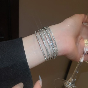 Macro shot of layered diamond bracelets on wrist holding a glass in elegant setting