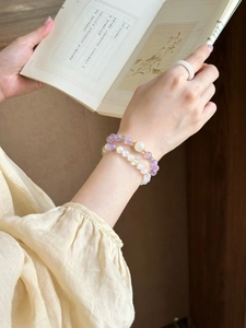 Detail view of amethyst and green stone beaded bracelets on wrist with aesthetic book