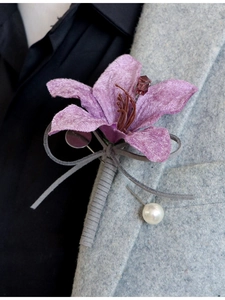 Detail of purple artificial lily boutonniere with silk petals and pearl pin on grey suit
