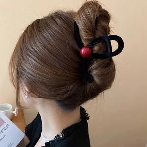 Detailed view of a black flocked hair claw clip with red beads worn on wavy brown hair
