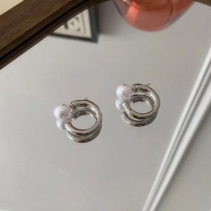 Detail view of silver C-shaped hoop earrings with pearls reflected on a mirror