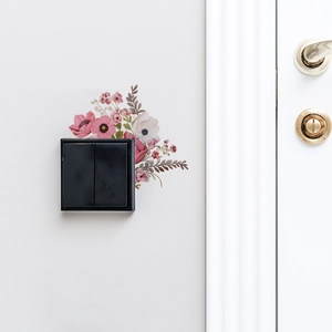 Pink and white flower wall sticker surrounding a black double light switch on a white wall