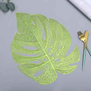 Green leaf-shaped PVC placemat with hollow design on grey tabletop with cutlery