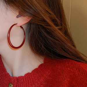 Close-up of a model wearing large glossy red hoop earrings with a vintage style