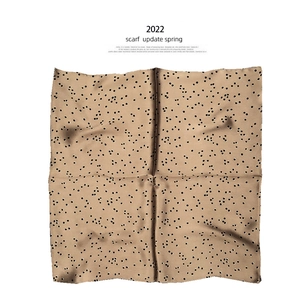 Detailed view of square silk scarf with black polka dots on brown fabric texture