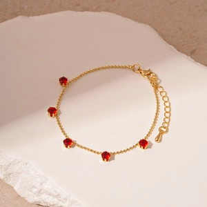 Detail view of gold bead chain bracelet with five round red stones and lobster clasp closure