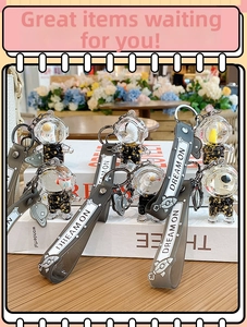 Detailed macro view of black astronaut liquid sand keychains with gold glitter and dream on strap