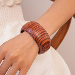 Detail of a wide wooden bangle with brown geometric stripes on a model's wrist