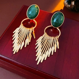 Vintage style gold earrings with green oval gemstones and elegant fringe detail on wood