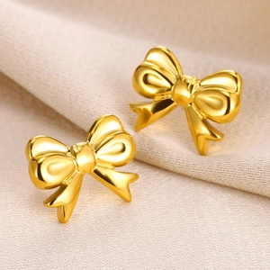 Detailed view of matte gold bow earrings featuring a textured 3D ribbon design on fabric