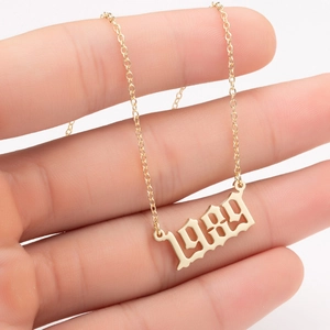 Macro view of gold stainless steel necklace with 1989 gothic pendant held by hand