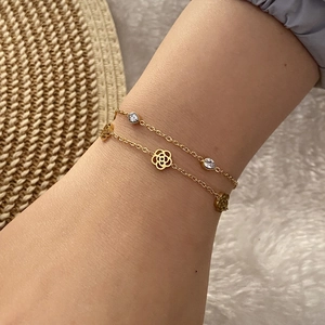 Close-up of double-layer gold chain bracelet with zircon and flower charms on wrist
