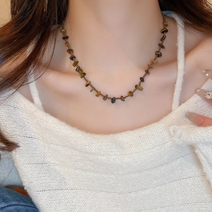 Détail d'un collier en pierre œil de tigre irrégulière sur un pull en maille blanc