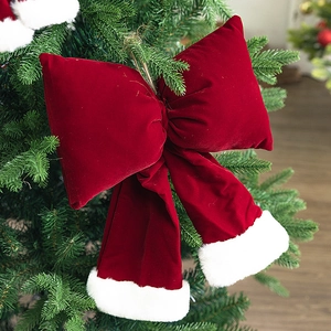 Large burgundy velvet Christmas bow with white fur trim hanging on a green Xmas tree