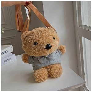 Detailed view of the brown plush bear crossbody bag wearing a grey hoodie on white desk