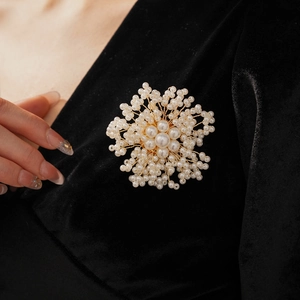 Close-up of handmade pearl flower brooch on black velvet fabric showing golden wire detail