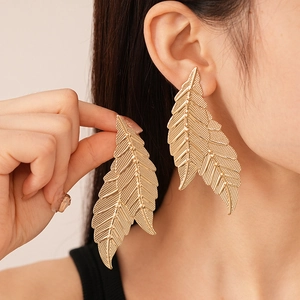 Detailed close-up of oversized golden leaf earrings with intricate vein textures on model