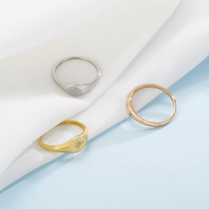 Three octagram signet rings in gold, silver, and rose gold on white silk fabric
