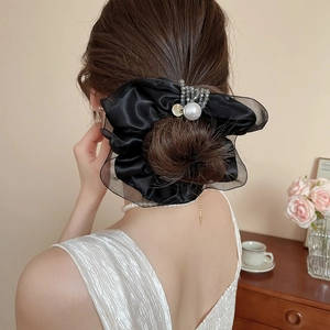Detail of elegant black satin and mesh scrunchie with pearls worn on a hair bun