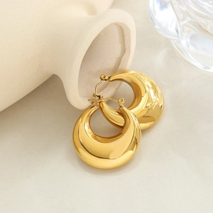 Polished gold U-shaped chunky hoop earrings leaning on a ceramic vase in warm light