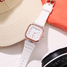 Square quartz watch with gold bezel and white silicone strap in a lifestyle setting