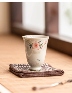 Detail of hand-painted peach blossom ceramic teacup on a woven mat with natural lighting