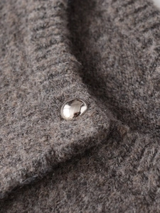 Nahaufnahme der silbernen Kugelknöpfe auf einer dicken, haferfarbenen Strickjacke