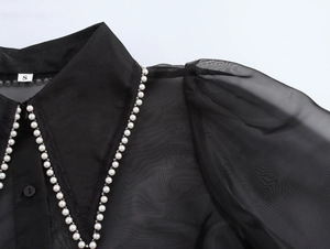 Close-up of elegant black organza blouse detailing pearl chain trim on collar and shoulder
