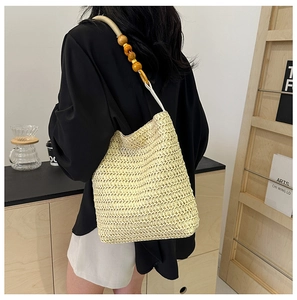 Detail of beige woven straw tote bag with large decorative wooden beads on strap