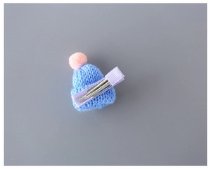 Detail of creative knitted mini hat hair clip with blue pompom and purple metal base
