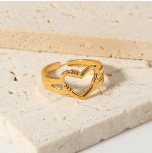 Close-up of golden hollow heart ring on a beige textured stone background
