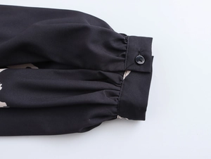 Close-up of black lantern sleeve cuff with beige vintage print and button detail