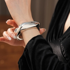 Close-up of irregular silver wave metal cuff bracelet on model's wrist with black velvet