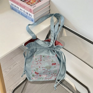 Detail of light blue denim tote with drawstring closure and cherry embroidery
